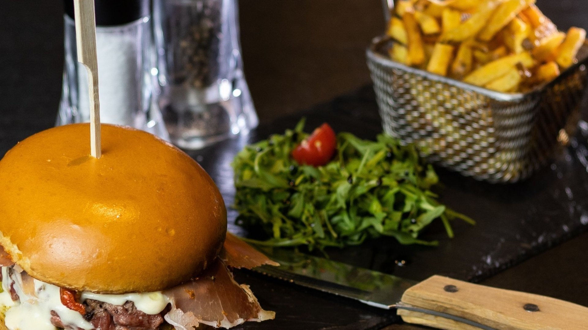 Un délicieux burger accompagné de salade et de frites, servi au restaurant L'Acacia du Casino Partouche Lyon Pharaon, pour une expérience gastronomique agréable.
